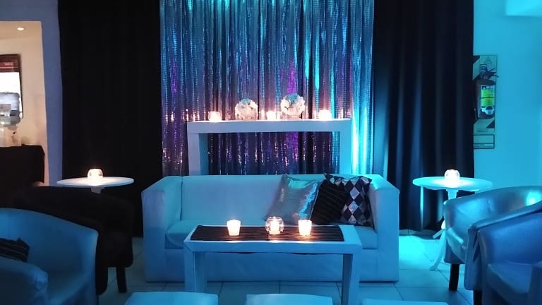 Zona lounge con sillones blancos y cortinas iluminadas en Metrópolis Espacio de Eventos